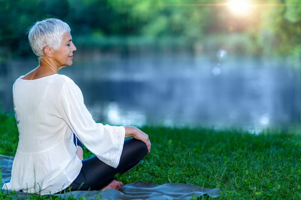 Senior woman meditating by the water